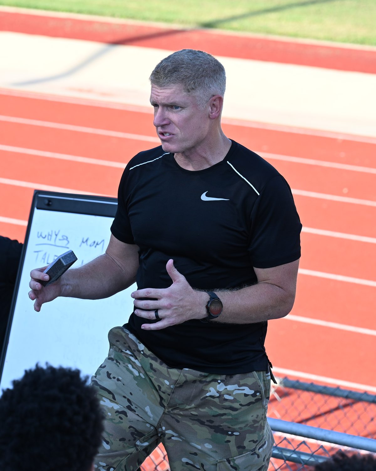 The founder, mid-sentence, talking with a group of young people beside a running track.